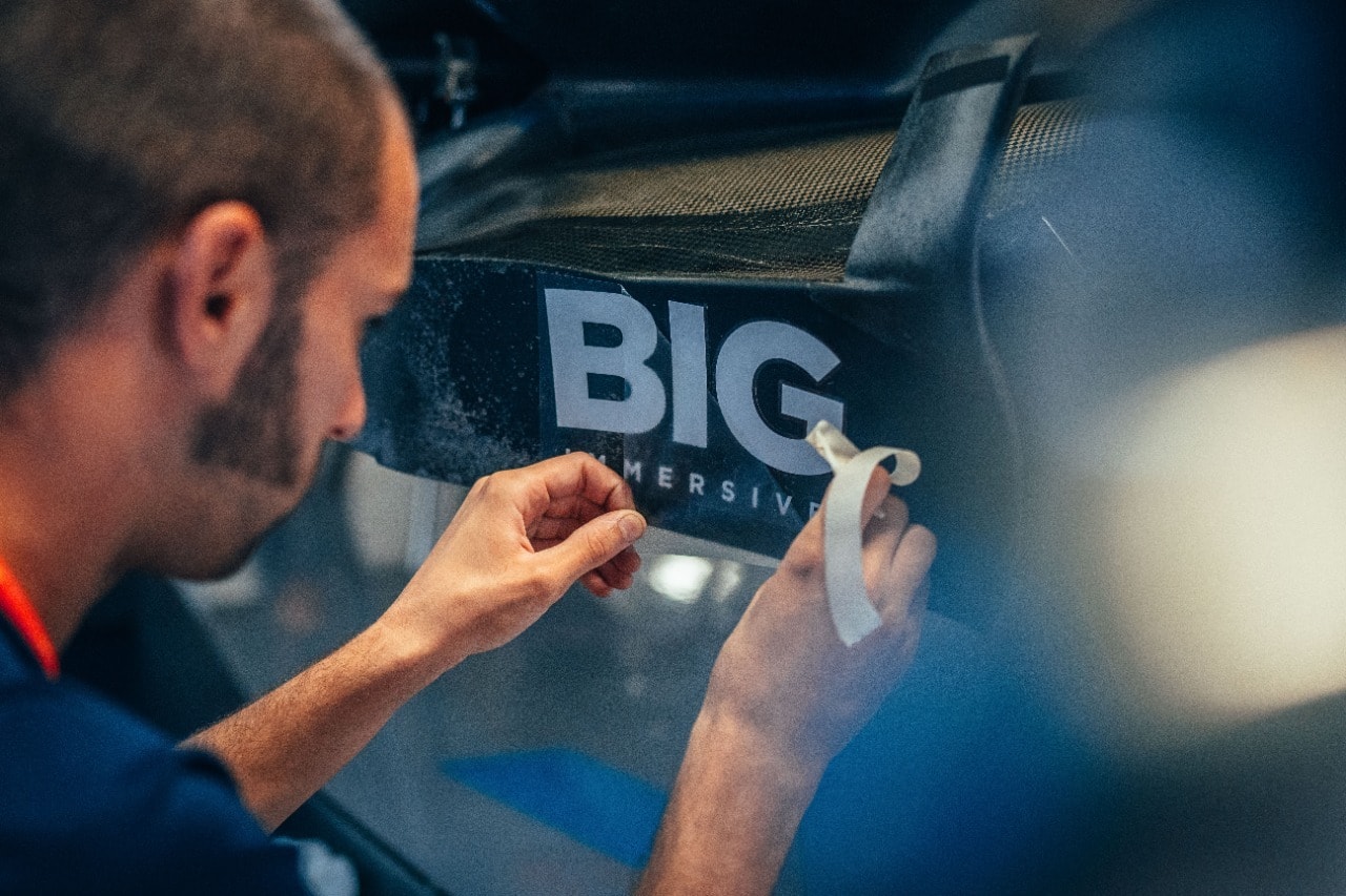 A Williams Racing team member applying the Big Immersive decal to the bodywork of the car in the garage.
